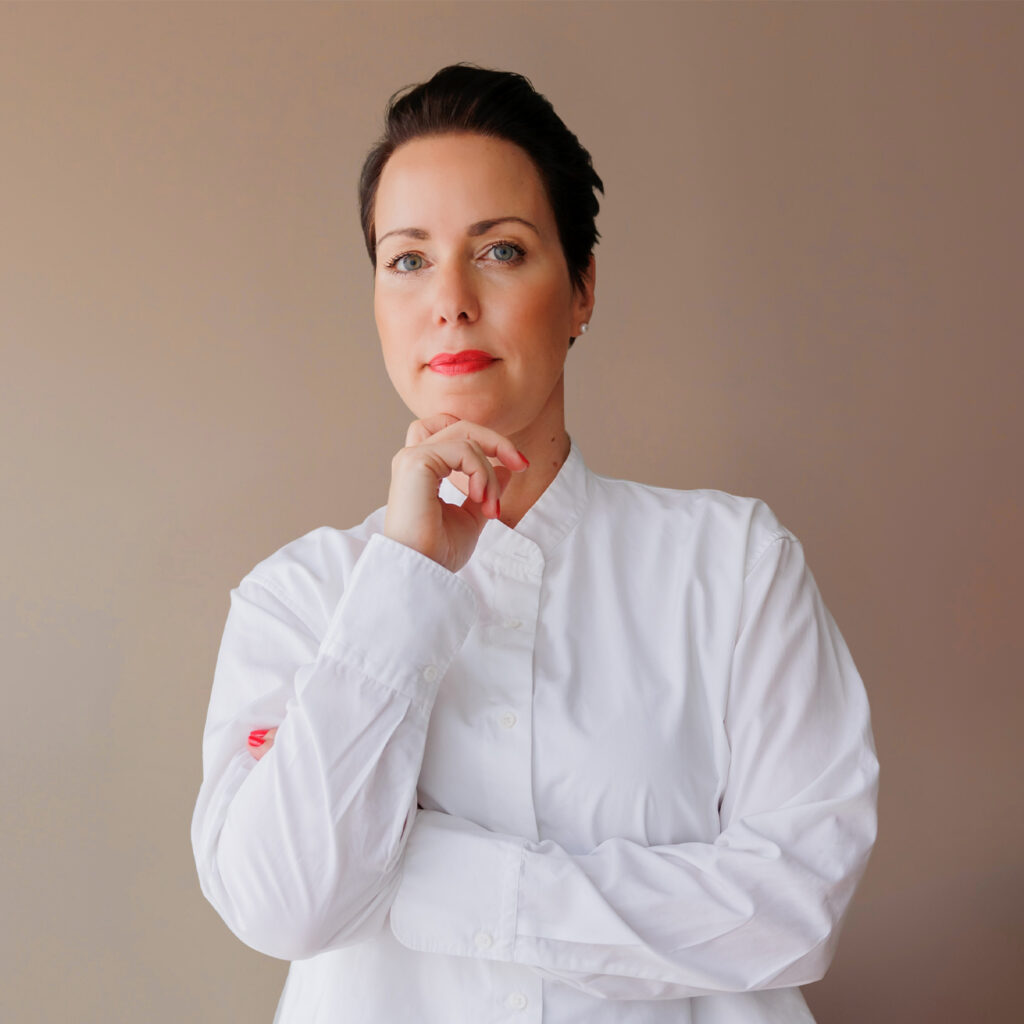 Person in weißem Hemd, nachdenklicher Ausdruck, stehend vor neutralem Hintergrund.