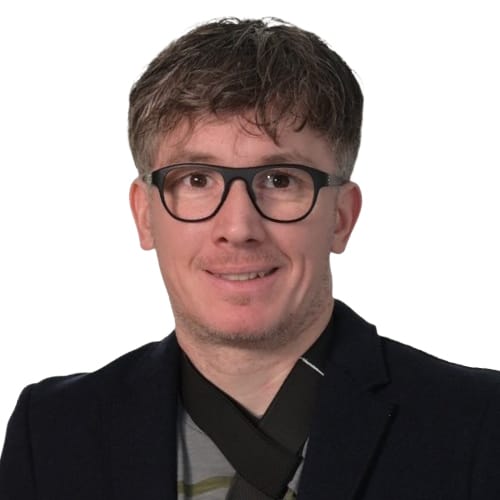 Porträt eines Mannes mit Brille, dunklem Blazer, lächelnd – professionelles Kopfbild.