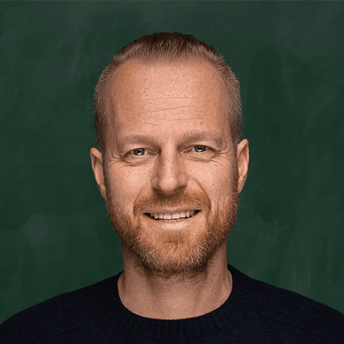 Porträt eines lächelnden Mannes mit rotem Bart vor grünem Hintergrund.