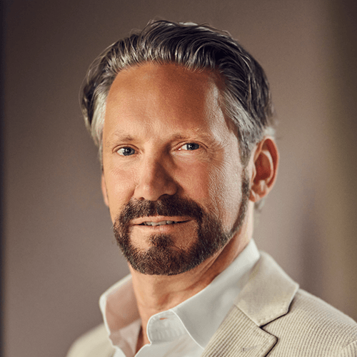 Professionelles Porträt eines Mannes mittleren Alters in hellem Sakko und weißem Hemd.