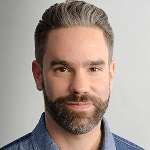 Porträt eines Mannes mit Bart und kurz geschnittenem Haar, Jeanshemd vor hellem Hintergrund.