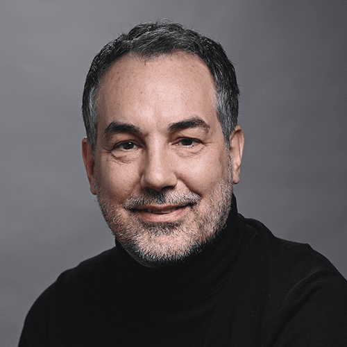 Porträt eines mittleren Alters Mannes in schwarzem Rollkragenpullover vor grauem Hintergrund.