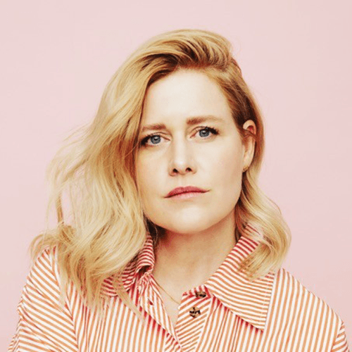 Nahaufnahme einer blonden Frau mit gestreiftem Hemd vor rosa Hintergrund.